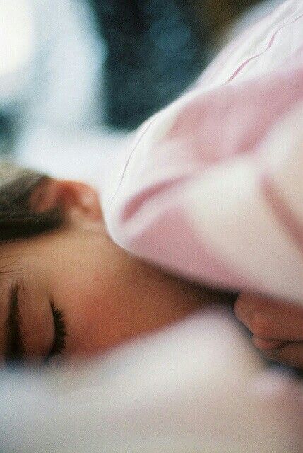A woman drifting off to sleep, eyes closed, face resting on a soft pillow