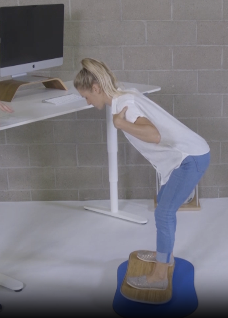 Hip hinge exercise on a FluidStance balance board at a standing desk, from Pop-Up Workout Episode 5
