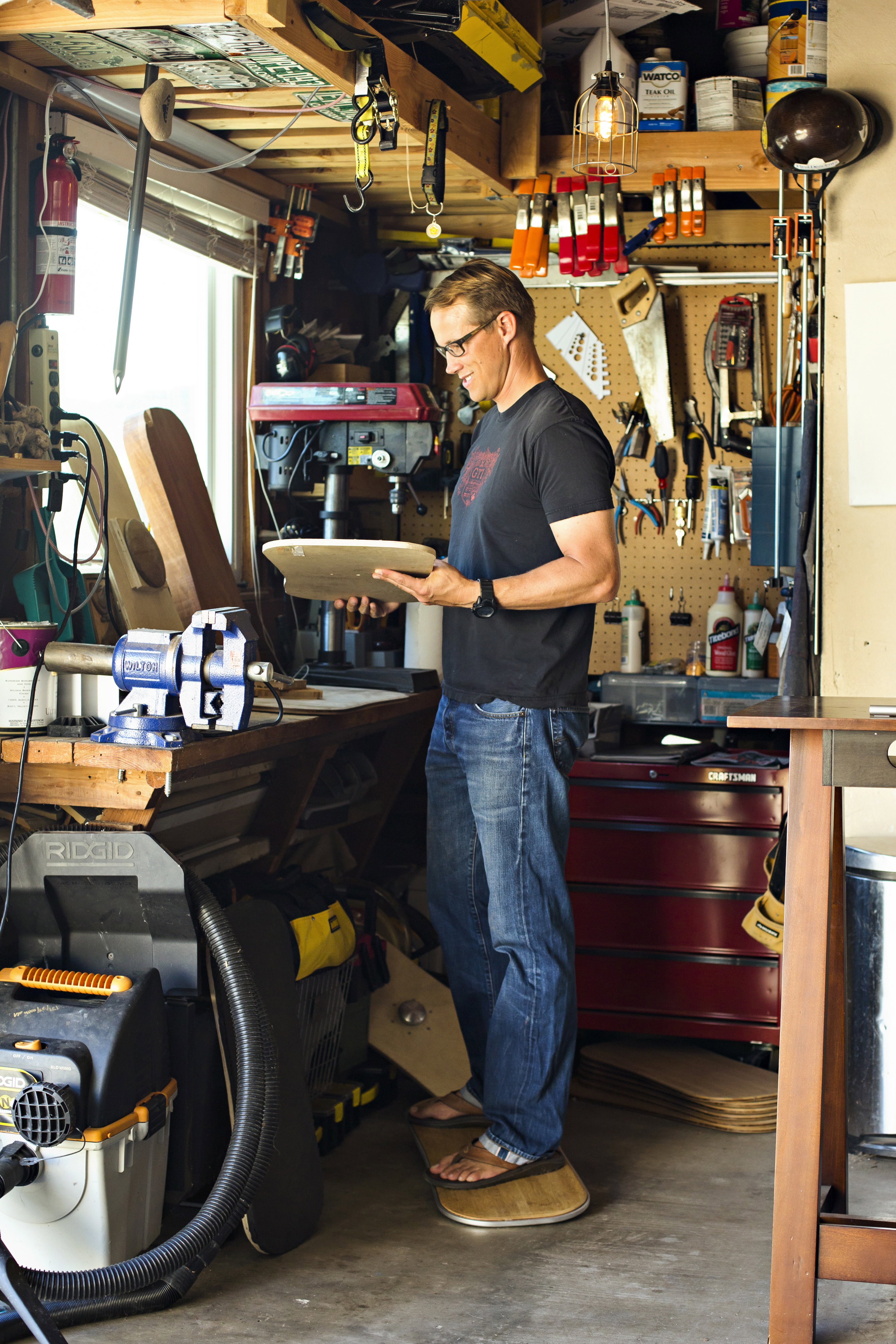 Man in his garage workshop inspecting a wooden board deck while standing on a balance board