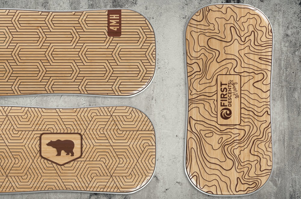 Three wood FluidStance top decks laser engraved with topographic contour lines, geometric patterns, a bear emblem and custom lettering, laid on a concrete floor