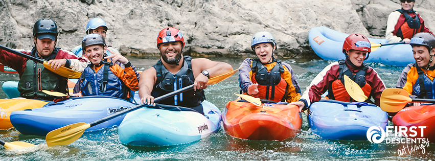 Smiling First Descents participants in helmets and life jackets sitting in colorful kayaks on a river