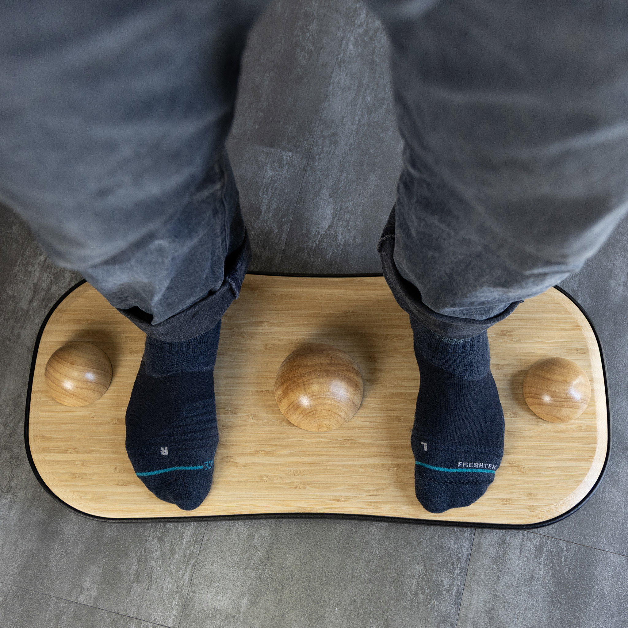 Feet in navy socks on a bamboo FluidStance balance board fitted with three Half Domes