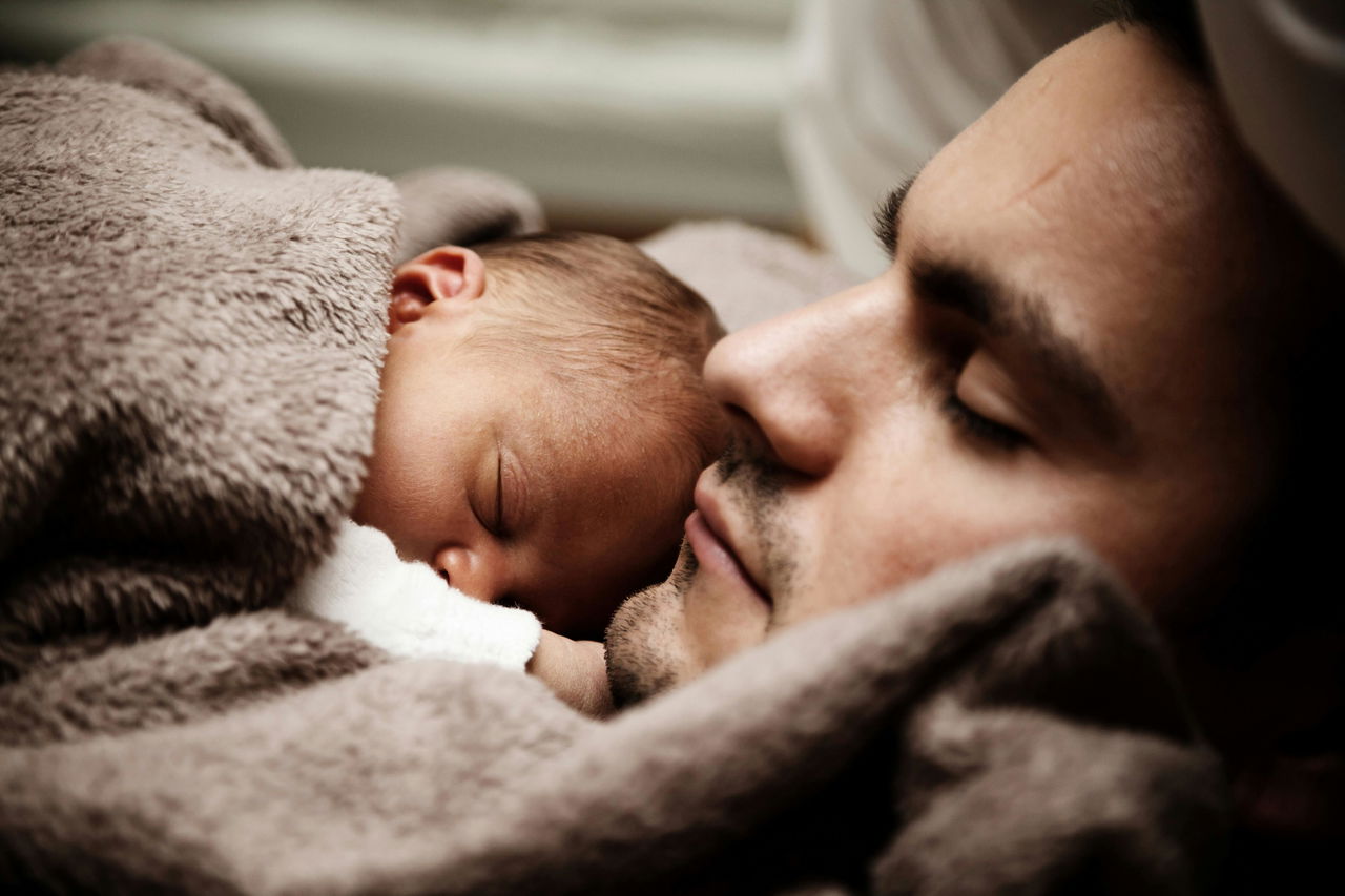 Liggende man met een slapende baby op zijn borst. De baby kan beter slapen bij zijn vader.