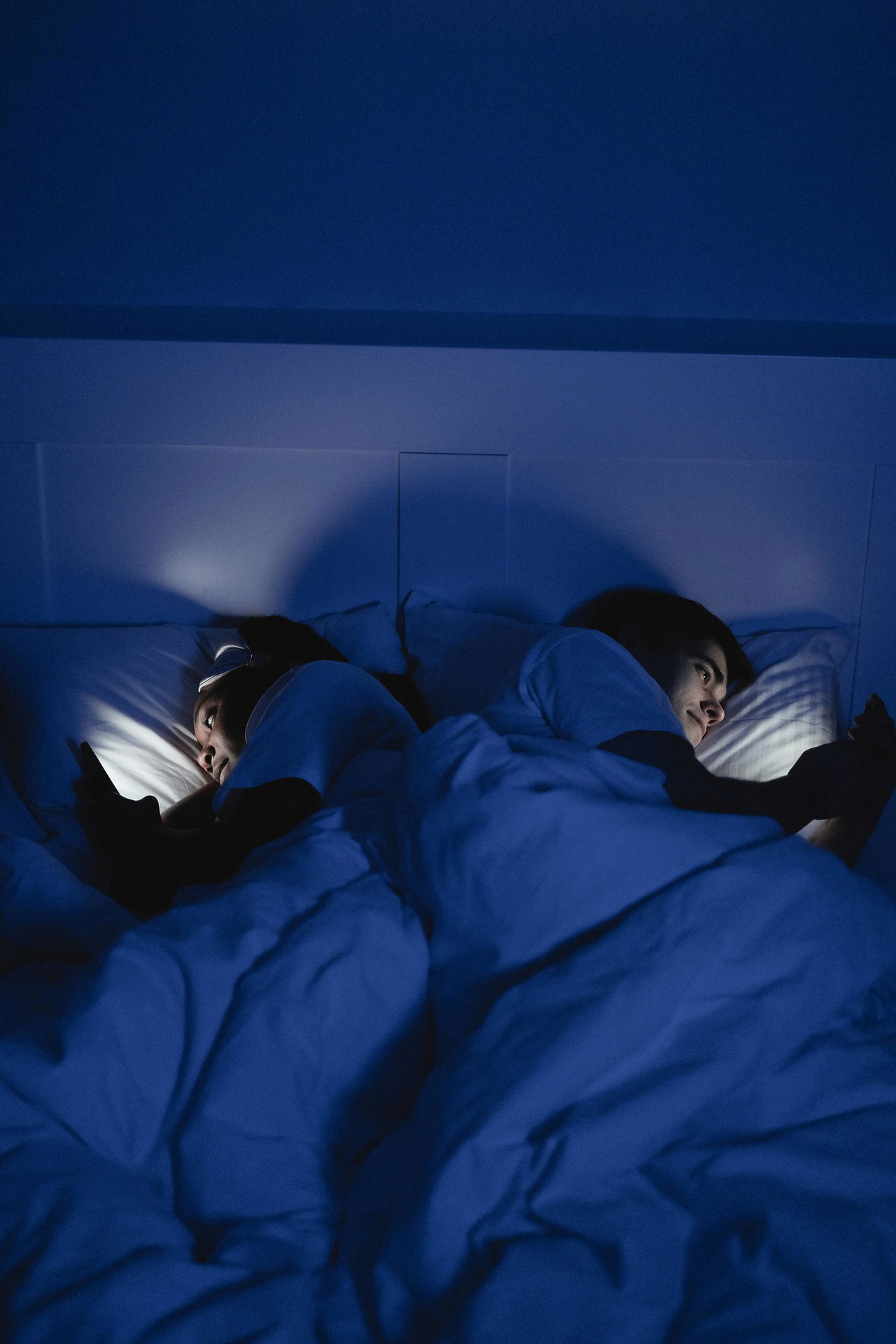Twee mensen in bed met slaapproblemen in bed die op hun mobiel zoeken naar slaapsupplementen.