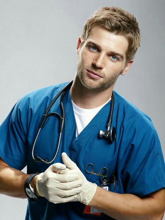Young male healthcare professional in blue scrubs with stethoscope and gloves.