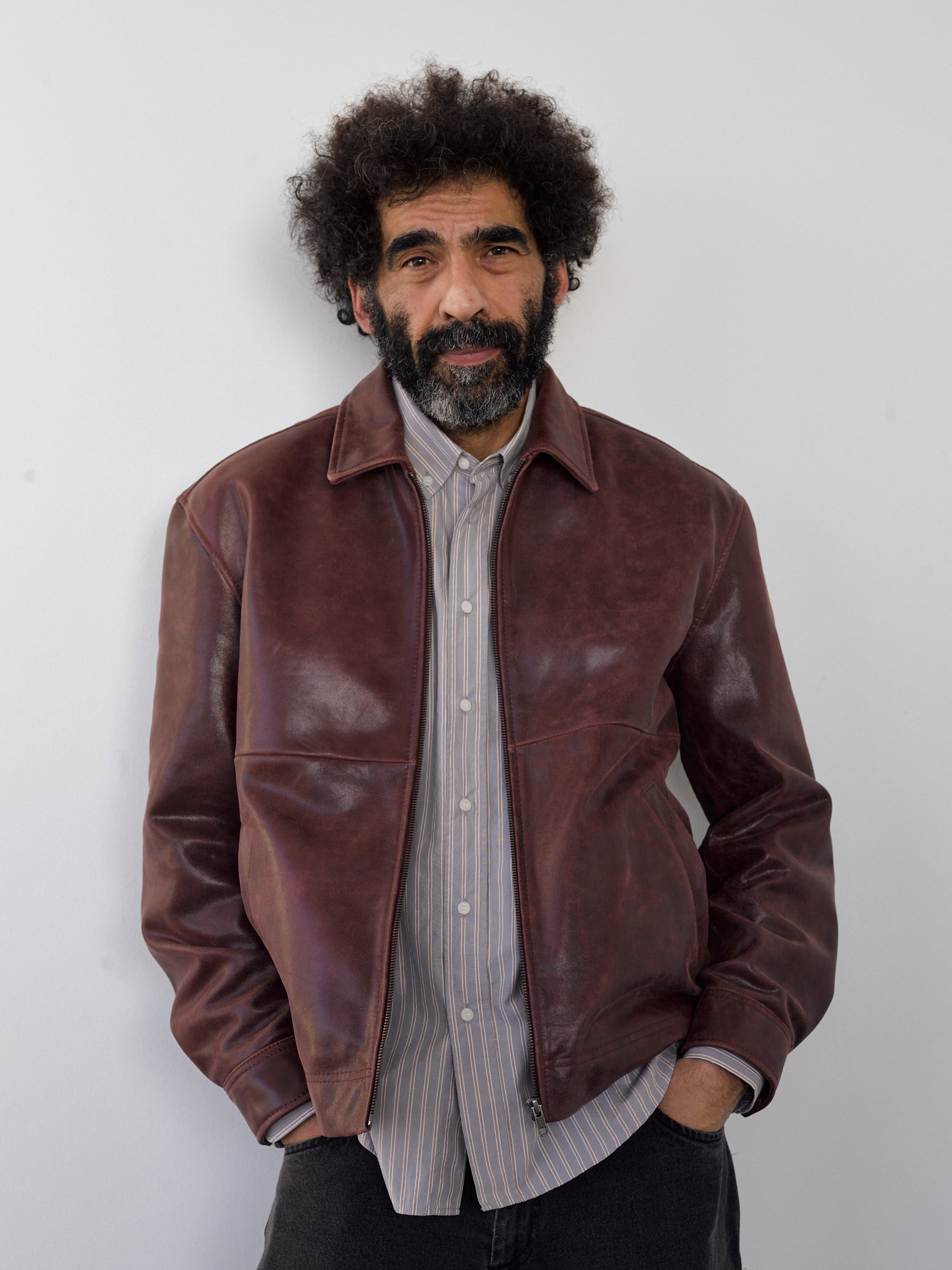 A burgundy satin shirt on a wooden hanger, resting on a concrete floor beside a stack of steel stools — Soulland AW26