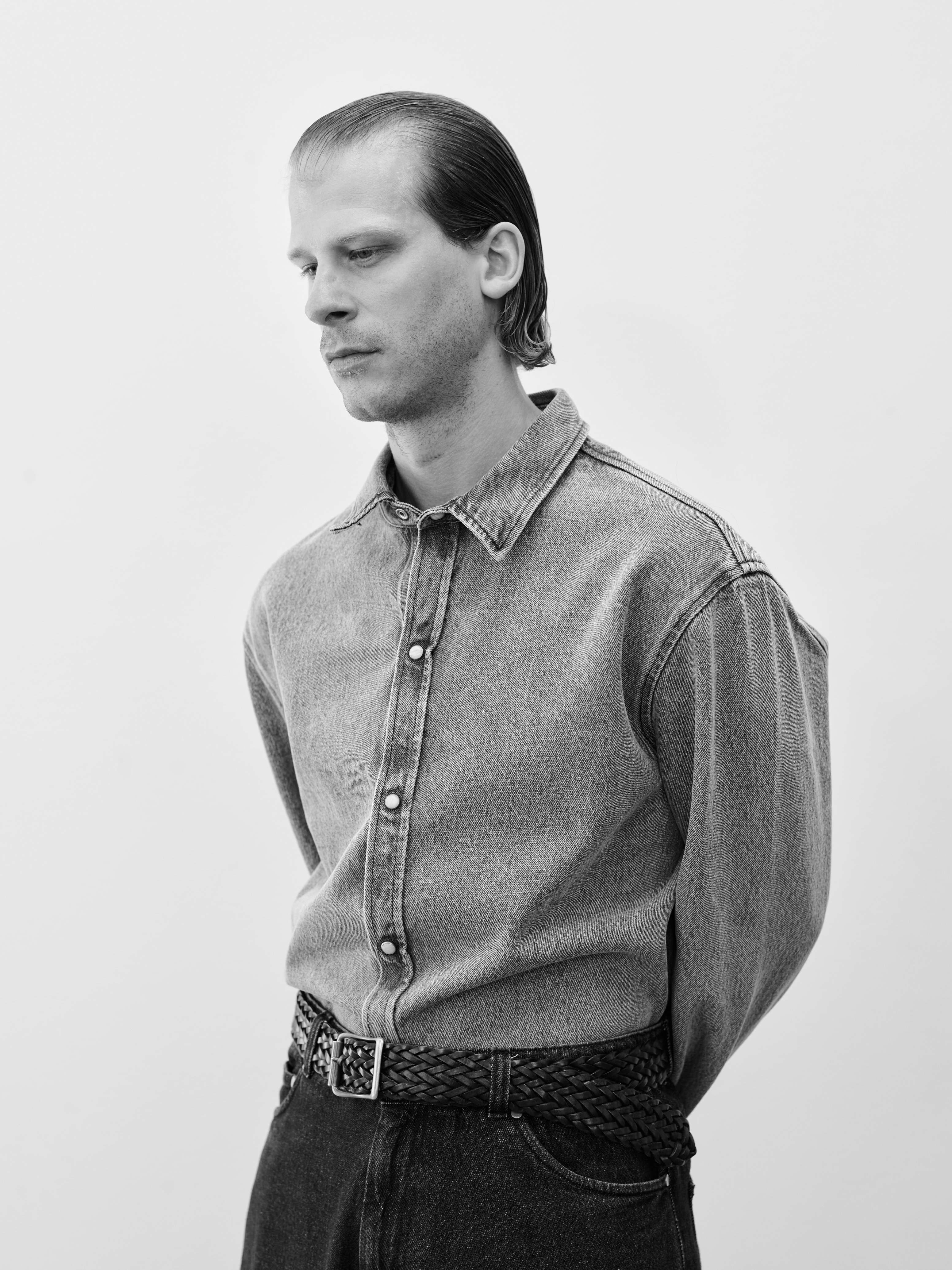 Model in a striped short-sleeve shirt and washed black denim against a white wall