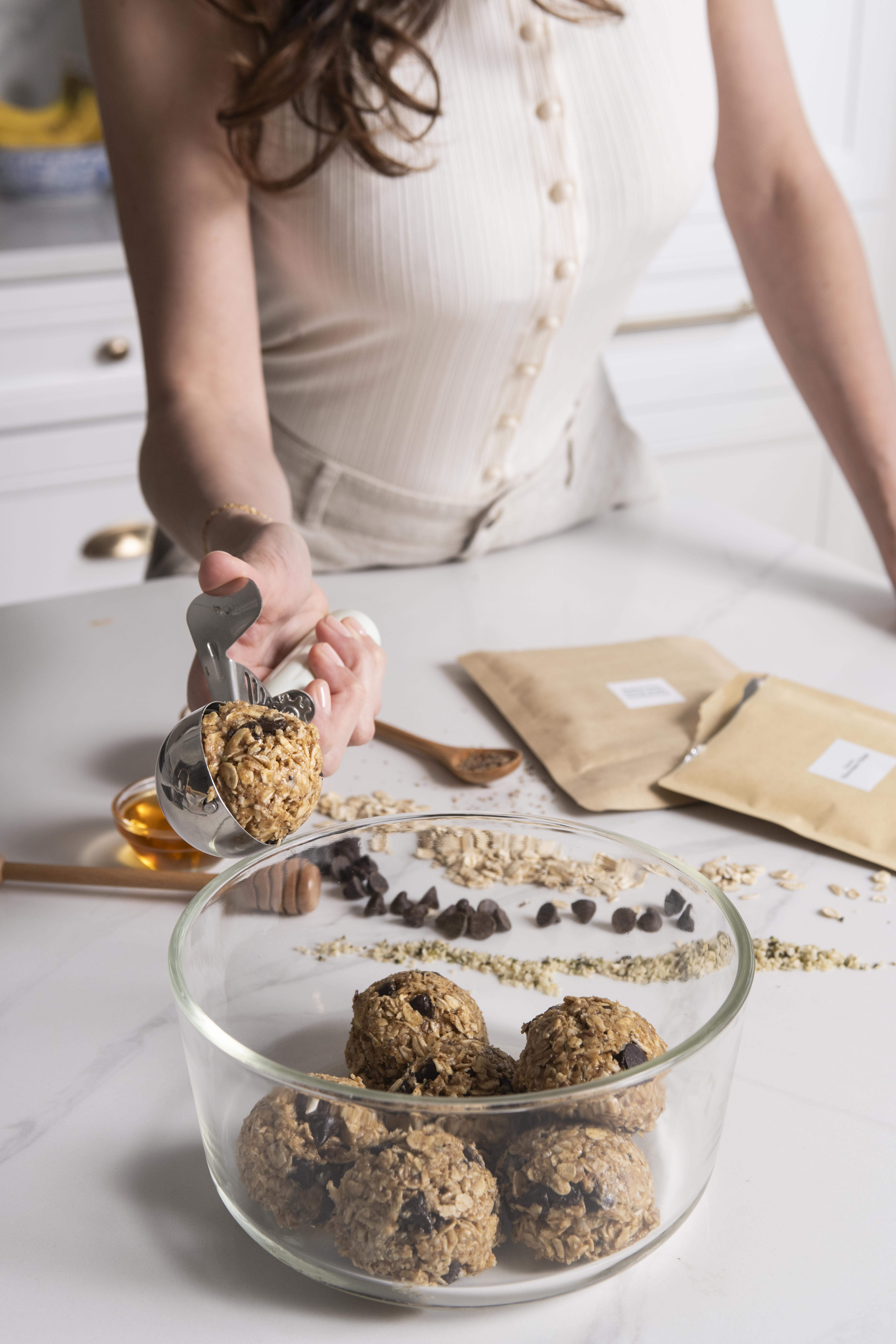 Hands rolling oat balls on a sunlit kitchen counter beside a plate of finished ones