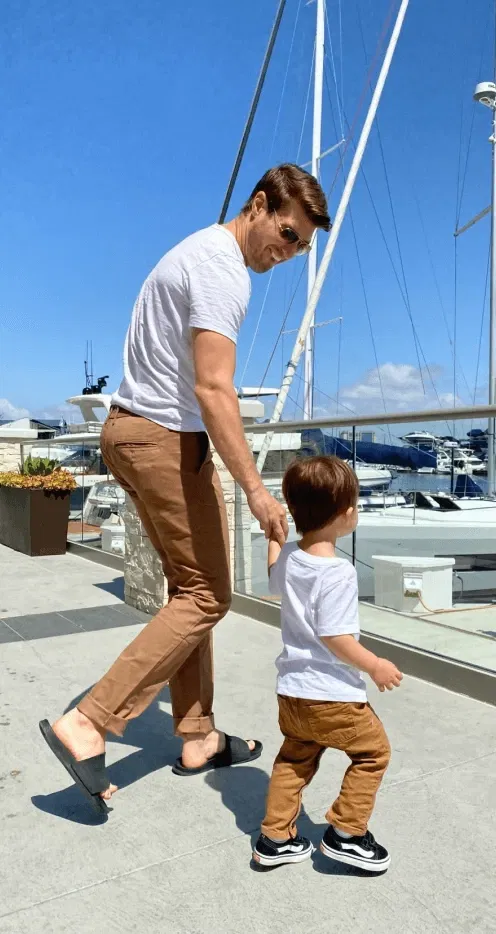 An adult and child in matching outfits walking by a marina with boats in the background.