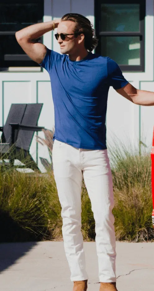 Man in blue shirt and white pants, standing outdoors, hand on head, wearing sunglasses.