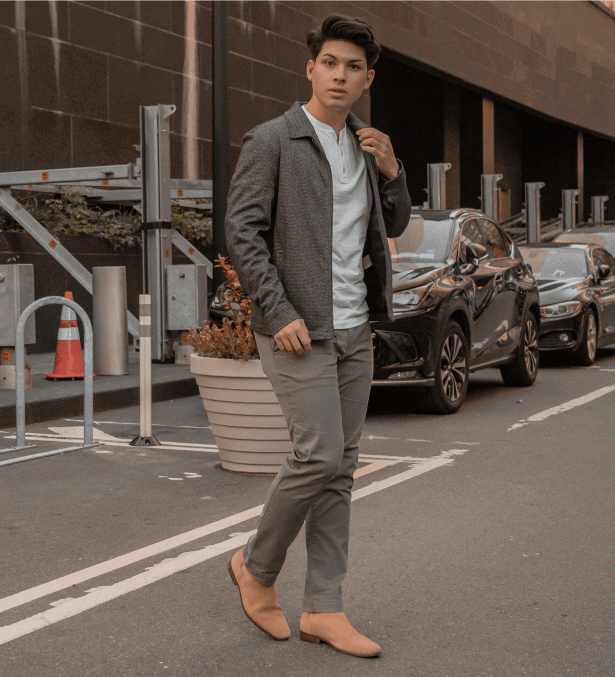 Man in gray outfit wearing a faded black chinos Perk walks on a street near parked cars and orange traffic cones.