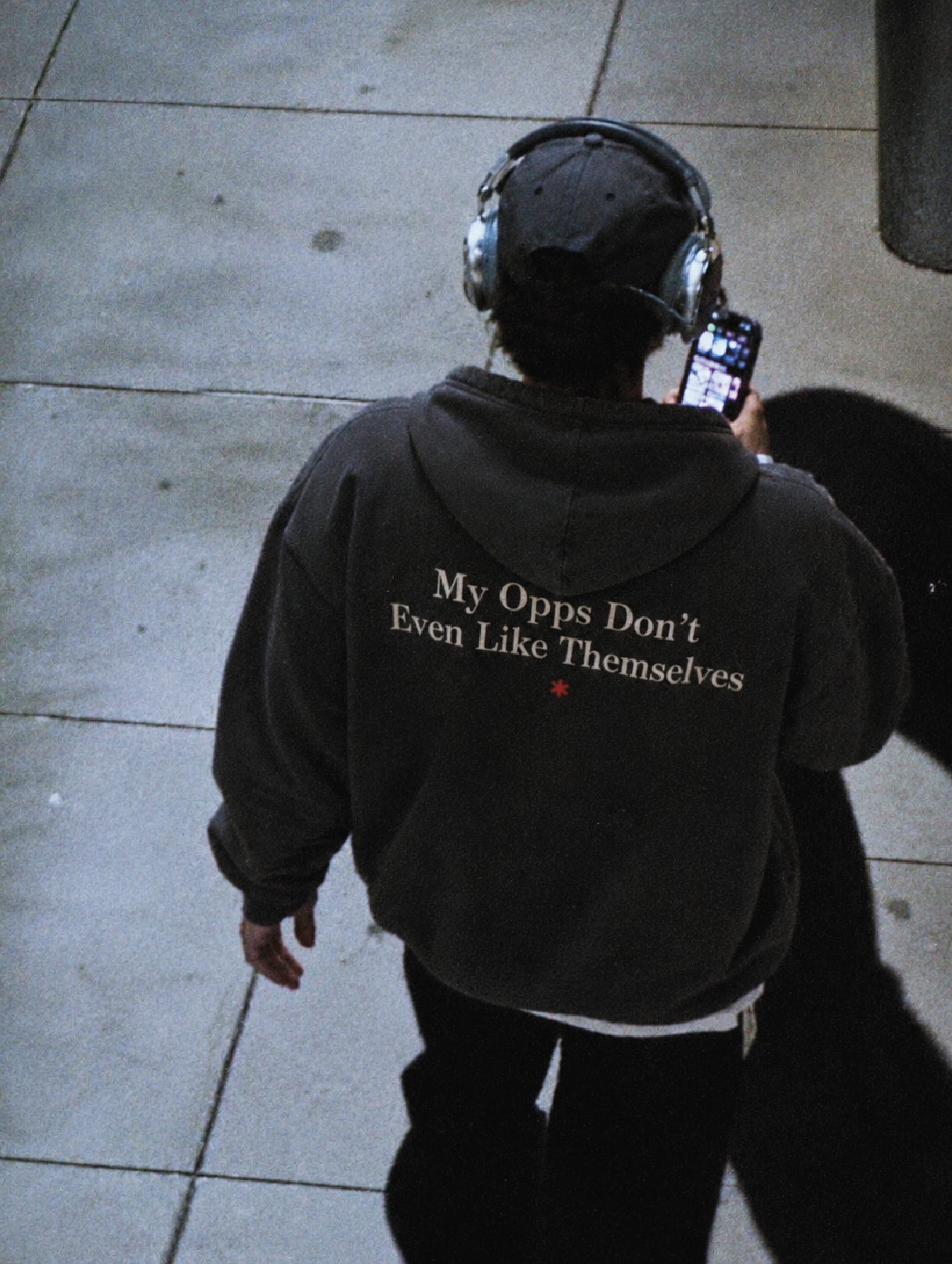 Overhead street shot of someone in headphones walking away, wearing the Opps Hoodie with the "My Opps Don't Even Like Themselves" back print