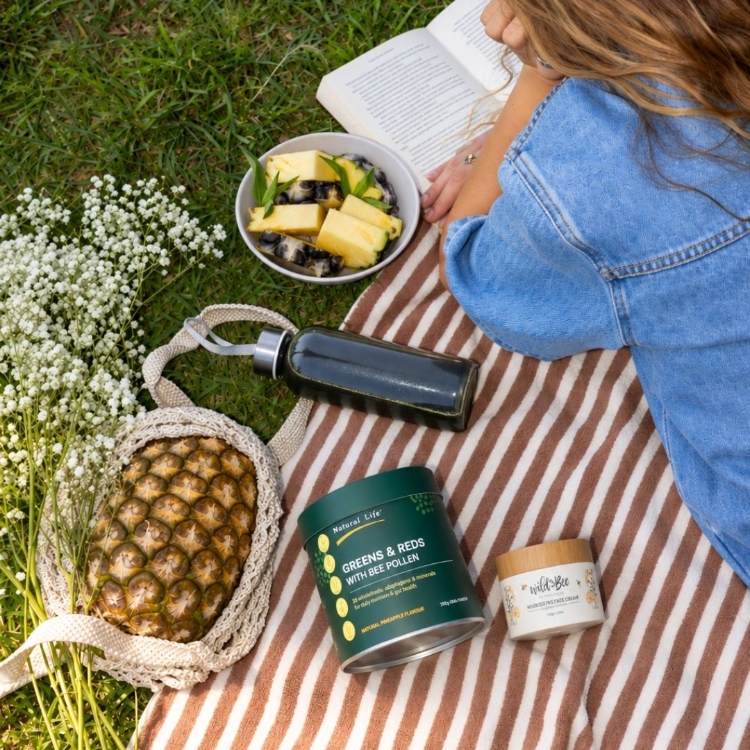 Greens & Reds with Bee Pollen on a striped picnic blanket with fresh pineapple and wildflowers