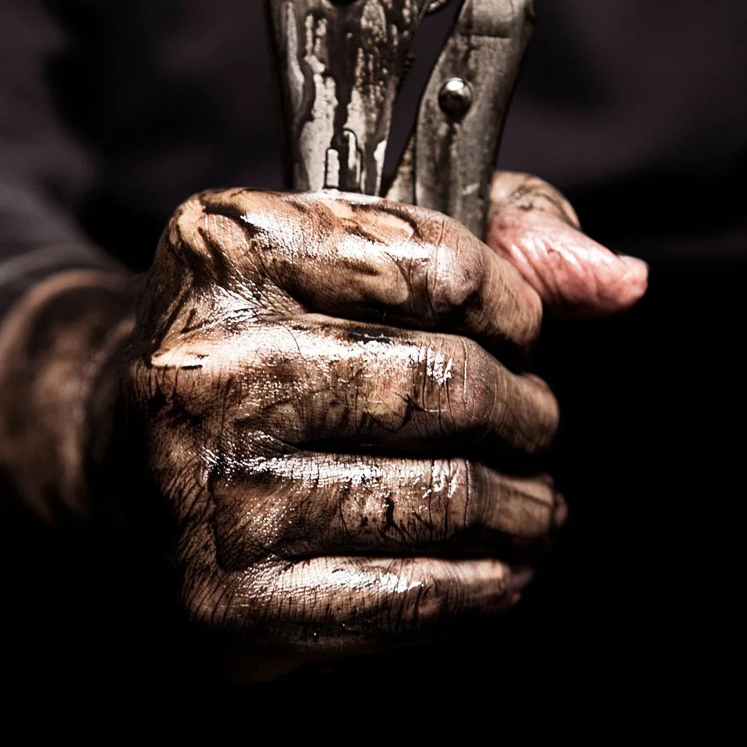 Grease-stained hand gripping wrench, deep cracks visible across dry knuckles.