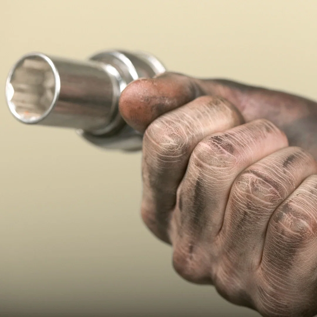 Close-up of a mechanic's dry, cracked hand gripping a chrome socket wrench.