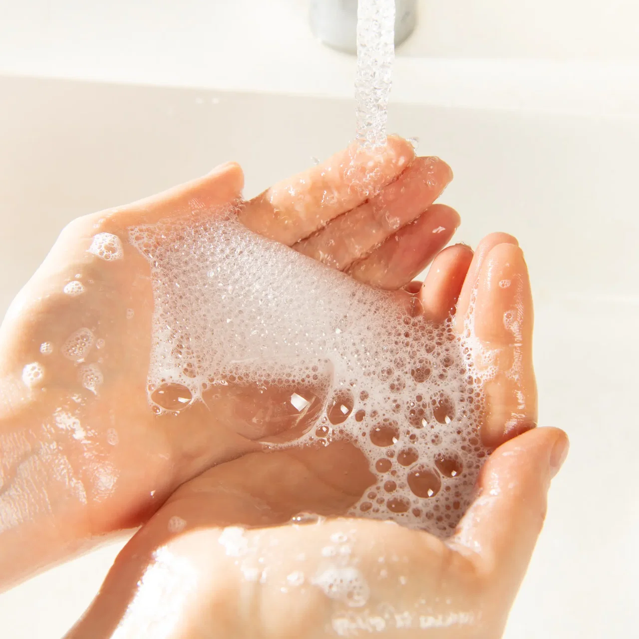 Hands lathered with soap foam under running water at a sink.