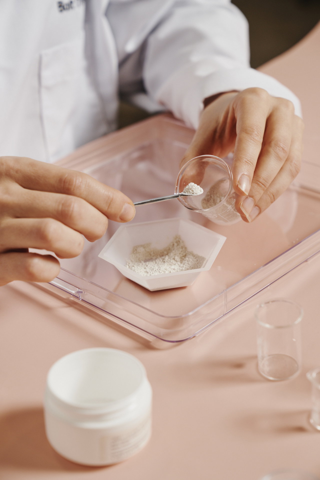 A lab technician in a white coat measuring white powder into a weigh boat with a small spatula representing B-silk™.