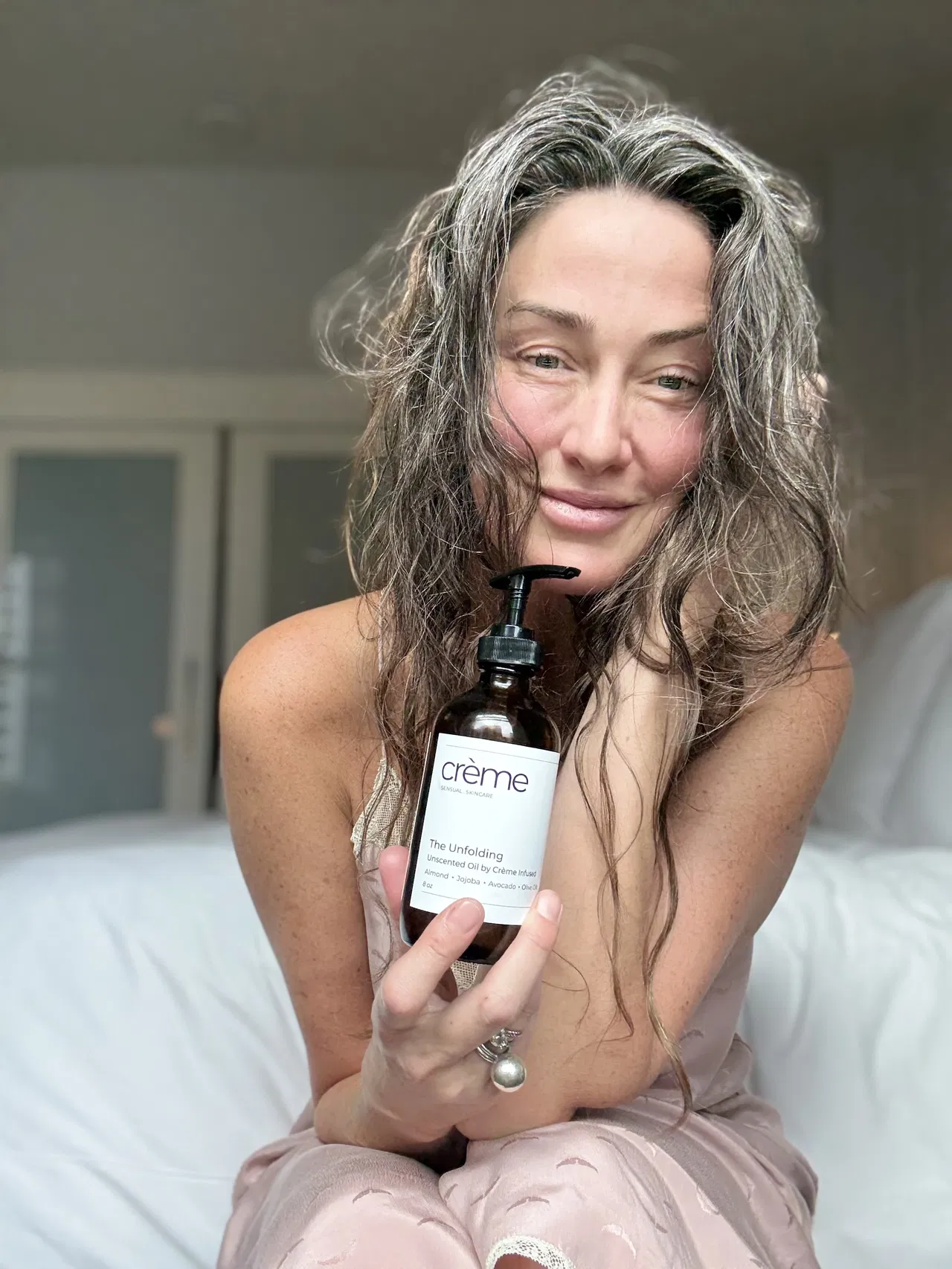Samantha Powell, Crème founder, holding The Unfolding Oil body oil with authentic smile representing midlife wellness
