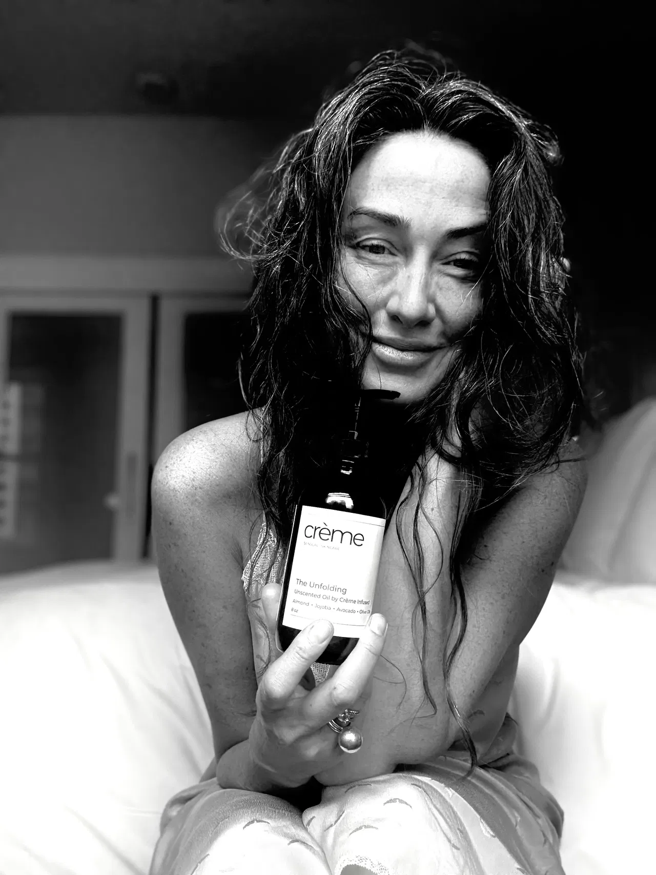 Samantha Powell, Crème founder, holding The Unfolding Oil body oil with authentic smile representing midlife wellness