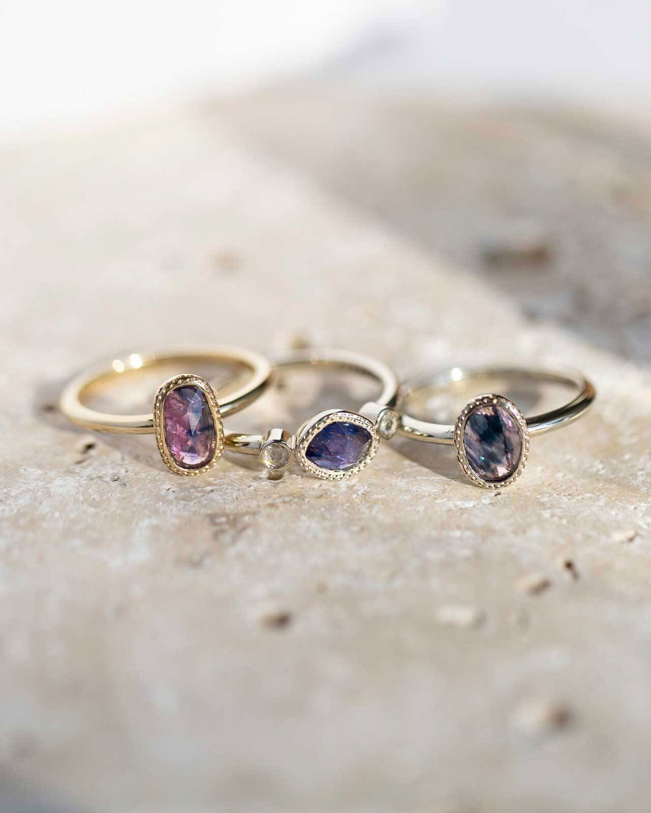 Close-up of three rose-cut sapphire stacking rings on travertine stone, handcrafted by Sara Gallo.	