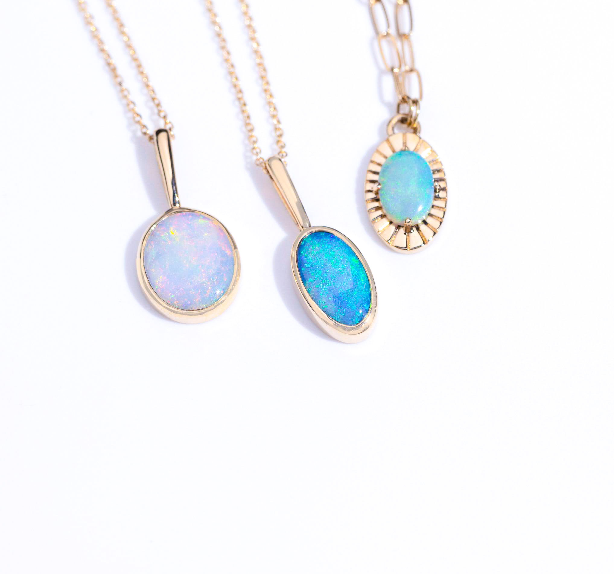 Three gold necklaces with oval opal pendants on a white background.