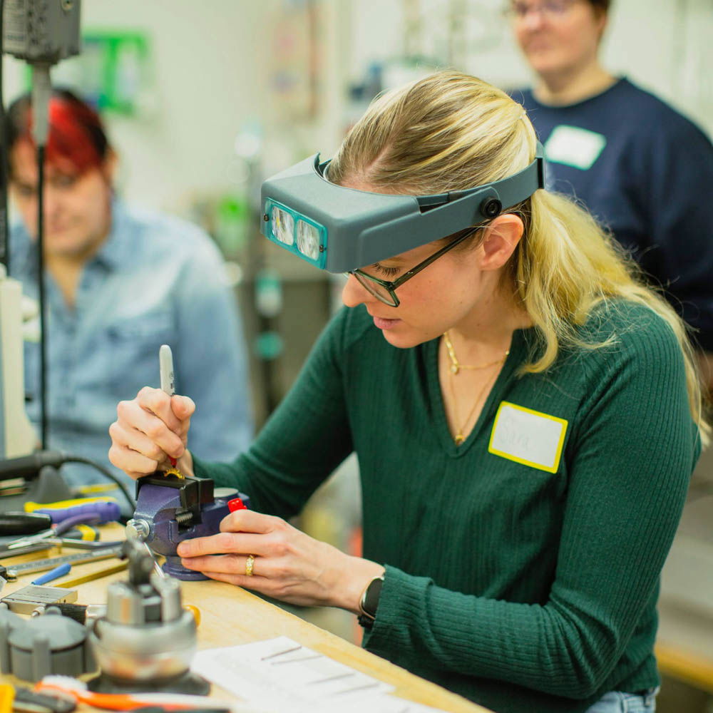 Sara Gallo wearing a magnifying visor demonstrates ring work at a busy jewelry-making workshop in Lancaster, Pennsylvania.