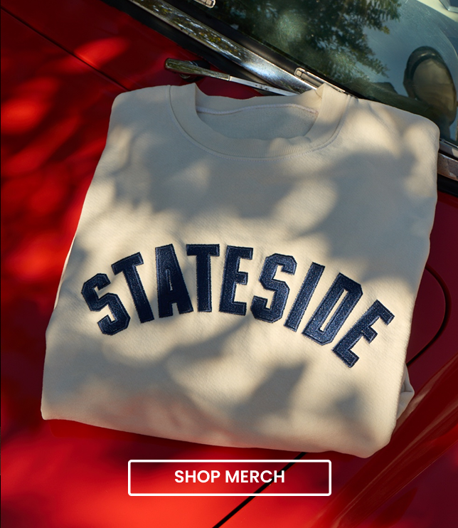 Cream Stateside crewneck sweatshirt with navy arched lettering laid on the hood of a red car in dappled sunlight