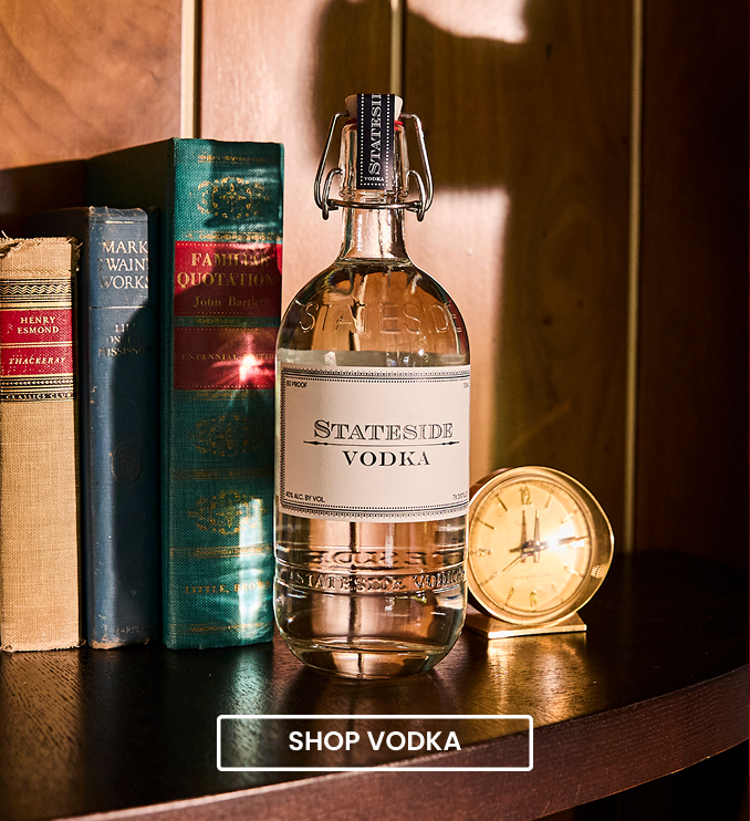 Stateside Vodka swing-top bottle on a wooden bookshelf beside vintage books and a brass clock