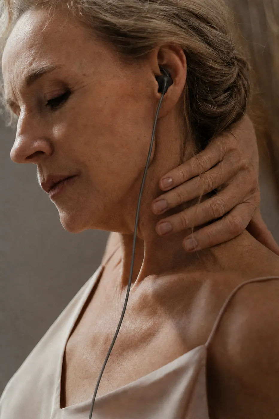 Woman wearing a black wired VNS ear stimulator earpiece while gently holding her neck