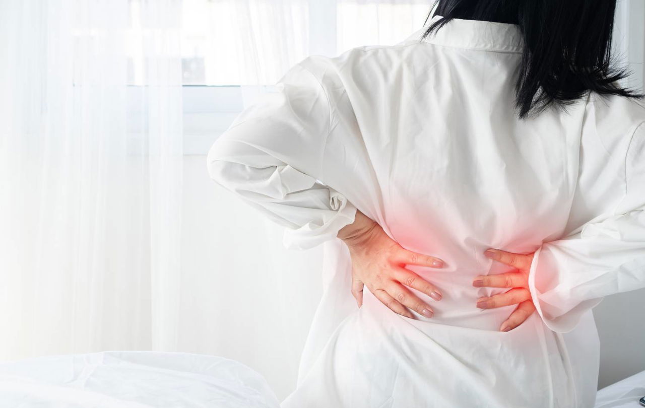 Person holding their lower back, wearing a white shirt, indicating pain or discomfort.