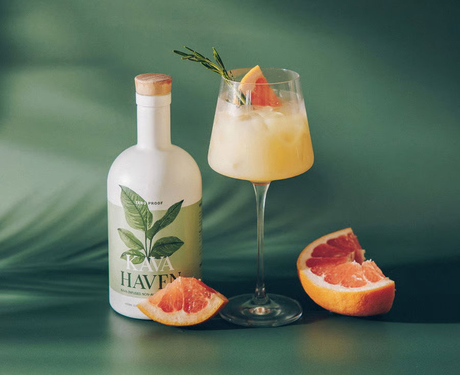 Golden Paloma in a stemmed glass with grapefruit and rosemary next to a bottle of Kava Haven