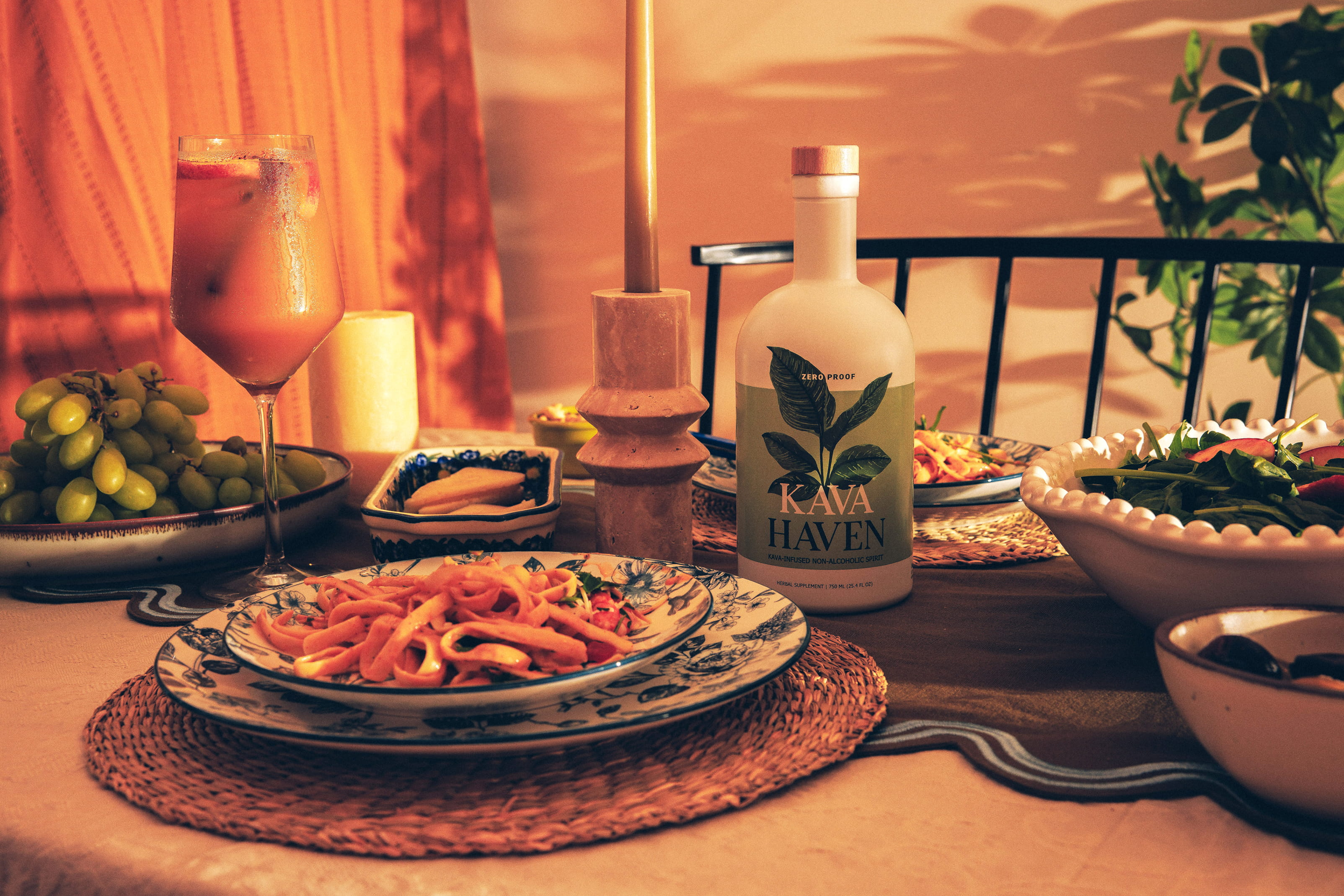 Kava Haven bottle and a glass over ice surrounded by lemon, white grapes, ginger, cardamom, orange blossom and vanilla