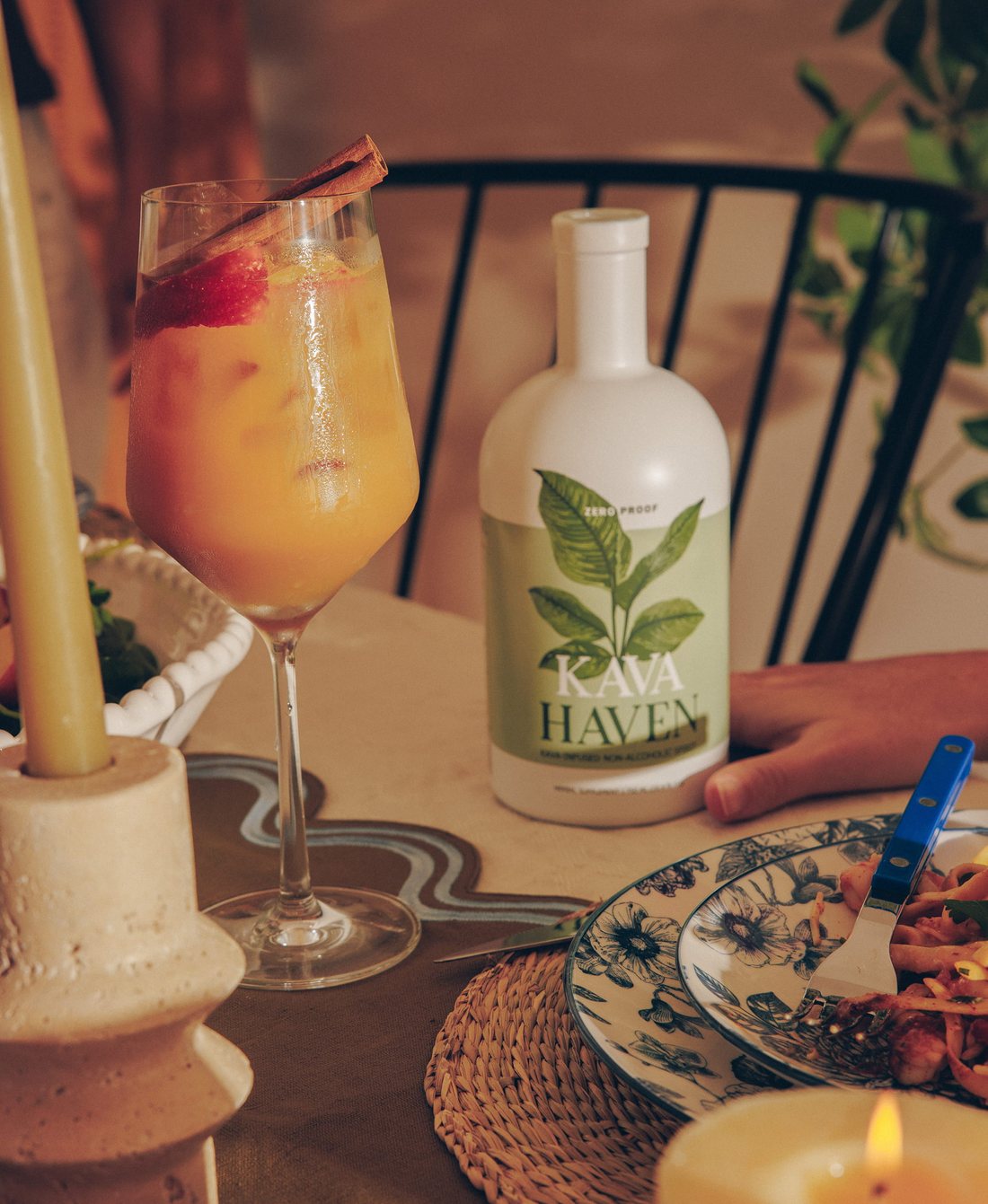 Citrus Kava Haven mocktail with a cinnamon stick beside the bottle on a cozy dinner table