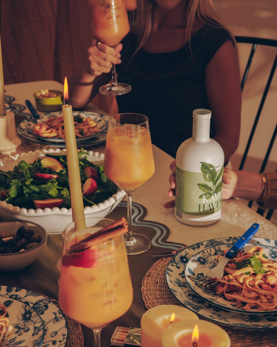 Kava Haven bottle on a poolside table with two iced citrus drinks at golden hour