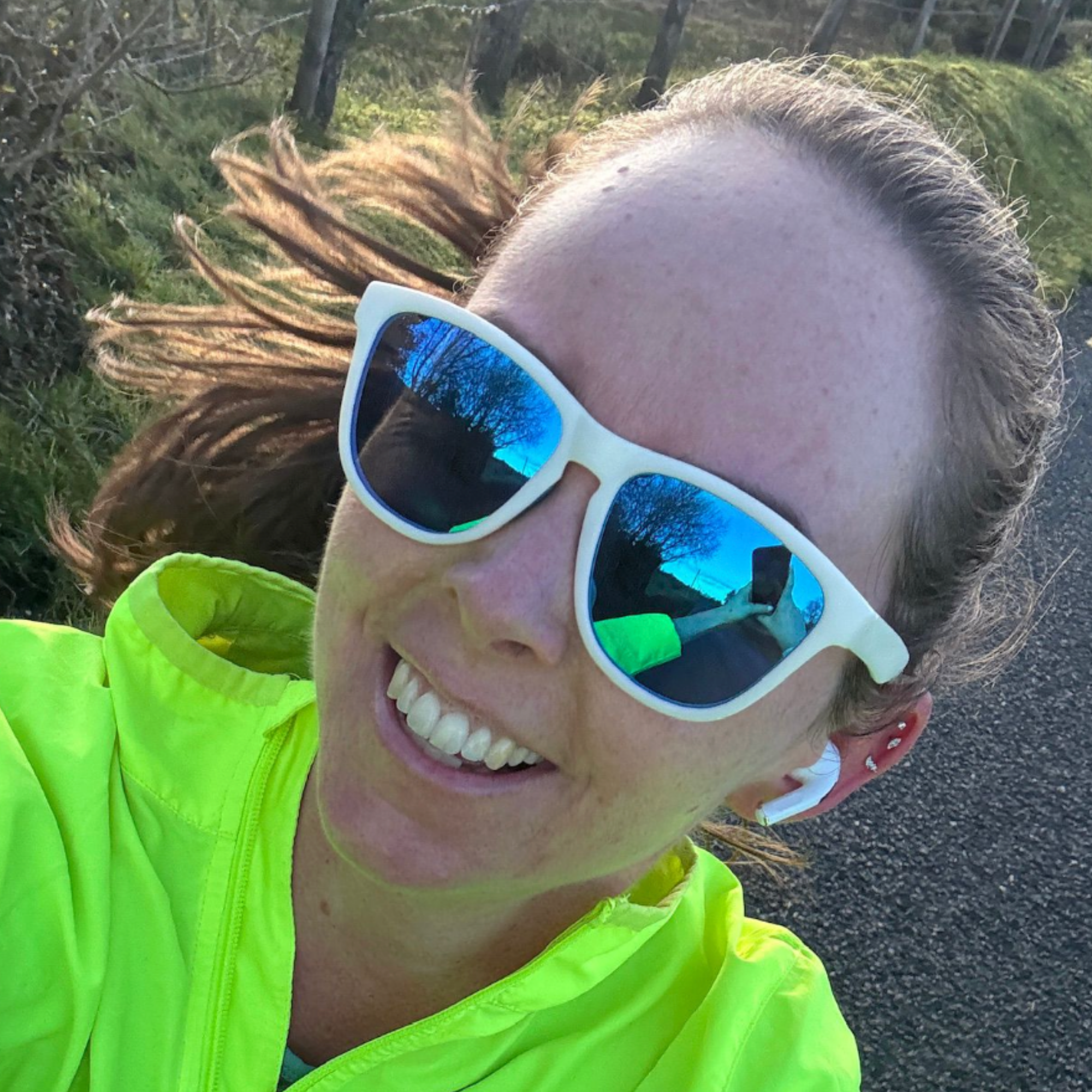 Smiling customer in a neon jacket taking a selfie outdoors in white H2OAthletics sunglasses with blue mirror lenses