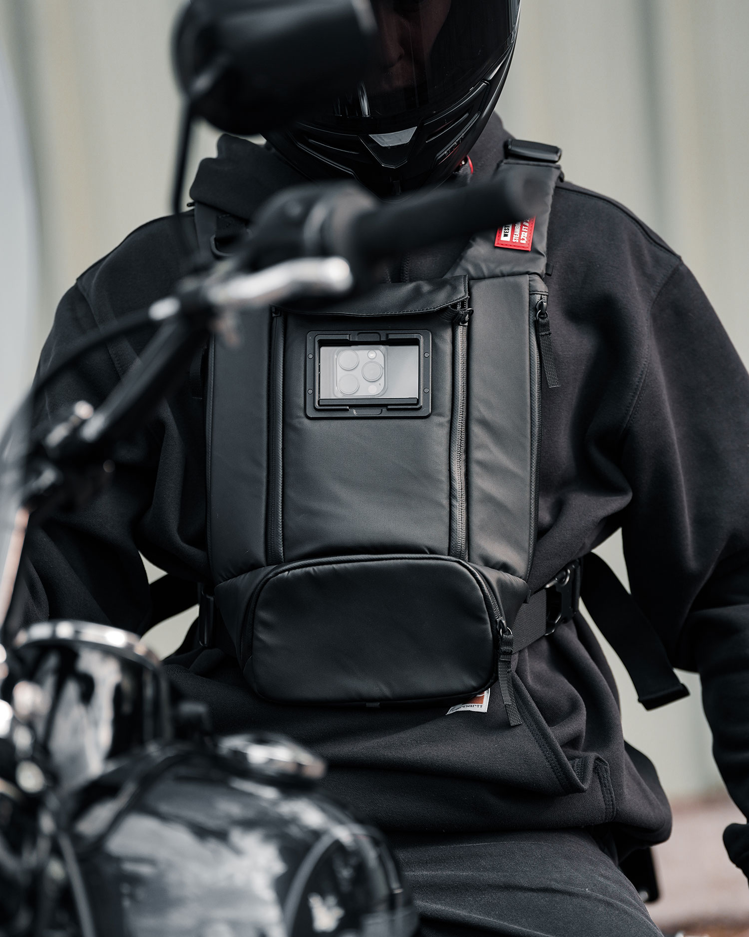 Motorcycle rider in a black helmet wearing a black West Slope chest pack with a phone visible in the front window