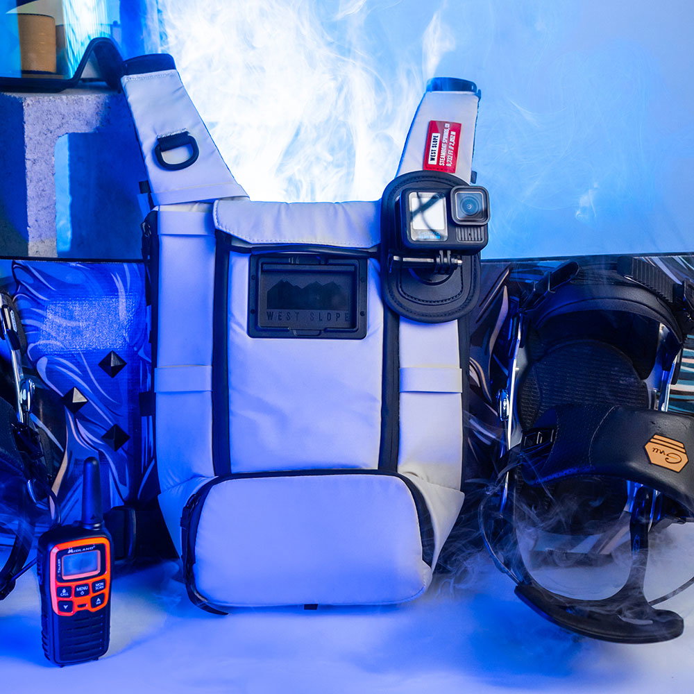 White West Slope chest pack with an action camera mounted on the Action Camera Kit plate, set between a snowboard binding and a two-way radio in icy blue fog