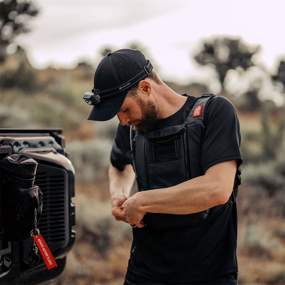 Rider in a black cap with a headlamp adjusting the strap of a black West Slope chest pack outdoors in the desert scrub