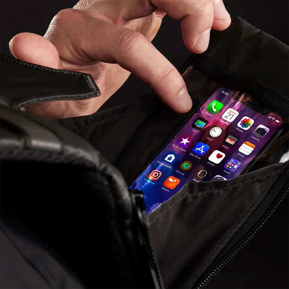 Close-up of a finger tapping a phone home screen through the clear front window of a black West Slope chest pack as the flap is pulled open
