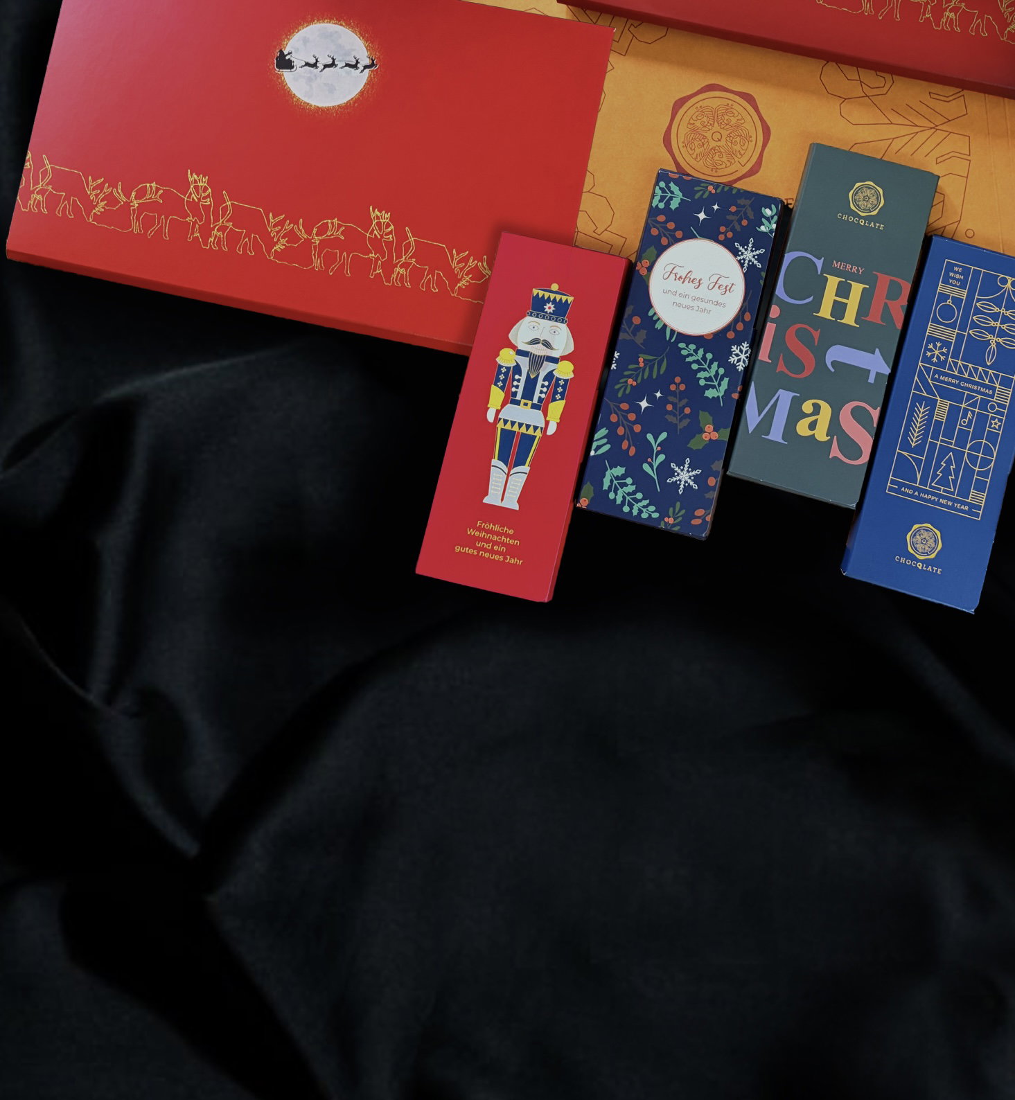 Rote CHOCQLATE Weihnachtsbox mit Mond und Rentieren, daneben vier weihnachtliche Schokoladen auf dunklem Stoff