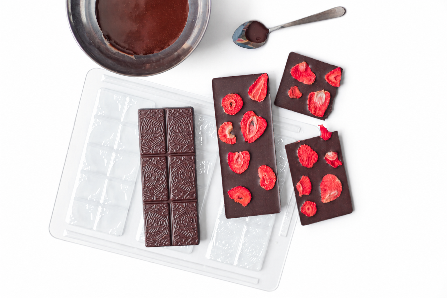 Selbstgemachte Schokolade aus der Form Ornamentik mit feinem Relief, daneben Tafeln mit gefriergetrockneten Erdbeeren
