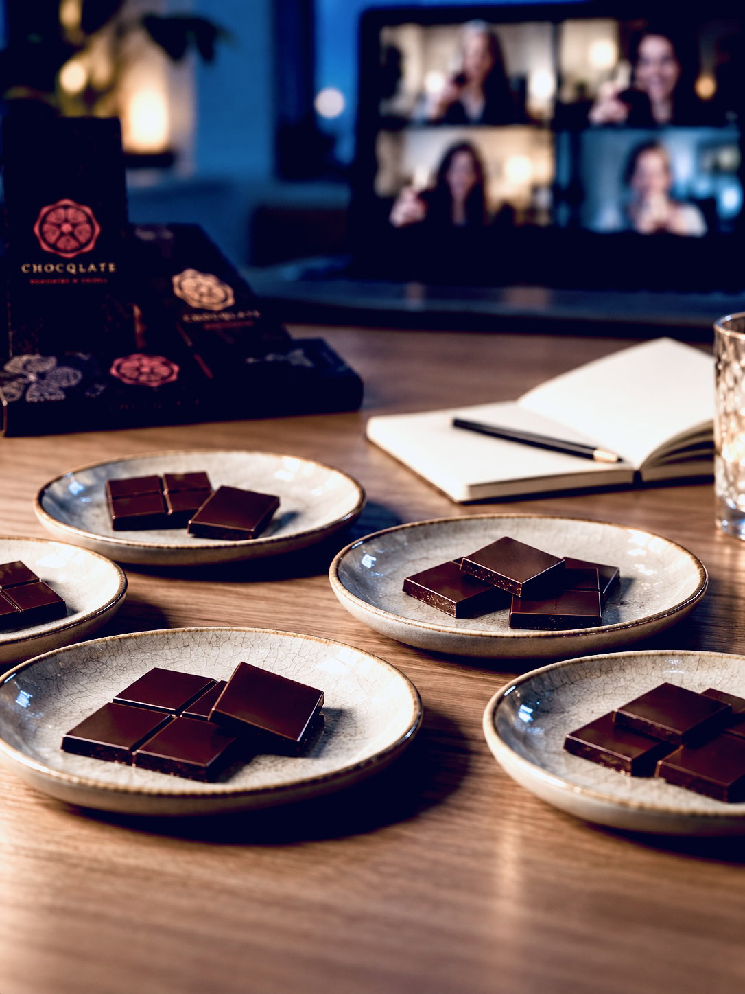 Tasting-Teller mit feinen Stücken dunkler CHOCQLATE Schokolade auf einem Holztisch, im Hintergrund die Teilnehmenden eines Live-Tastings auf dem Laptop