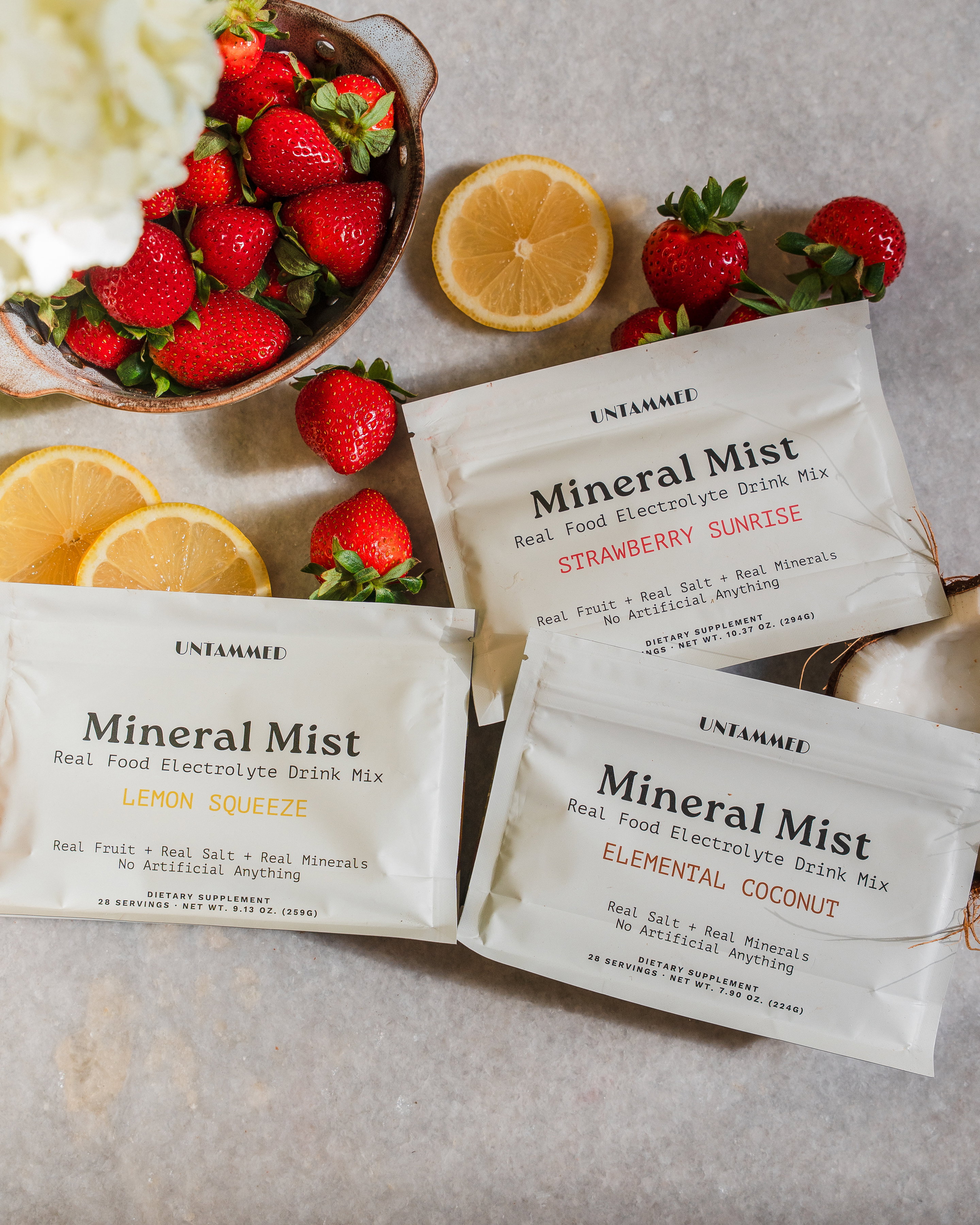 Lemon Squeeze, Strawberry Sunrise and Elemental Coconut Mineral Mist pouches with fresh strawberries and lemon slices