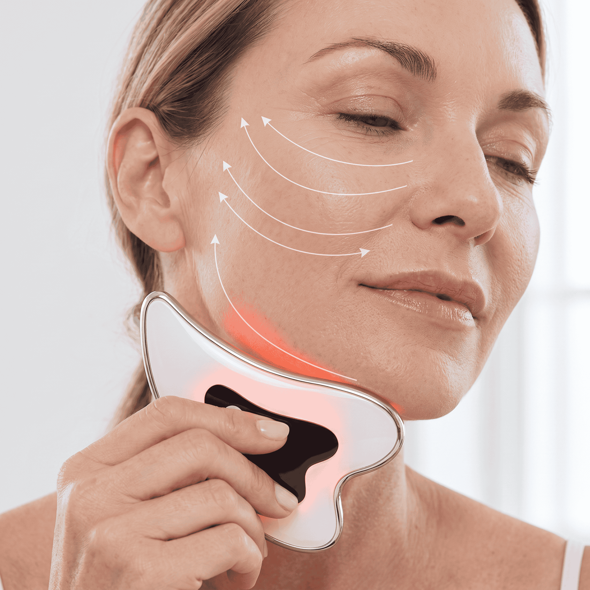 A woman gliding the warm gua sha device along her jaw, with red light on and arrows showing the upward stroke direction