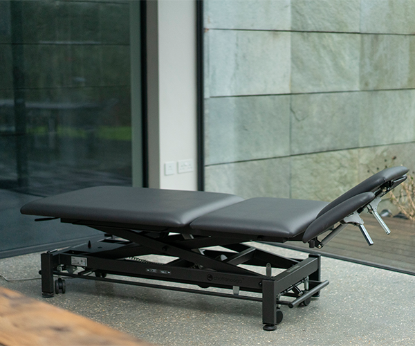 Table de soins Chattanooga noire à réglage électrique de la hauteur, devant la façade moderne d'un cabinet médical