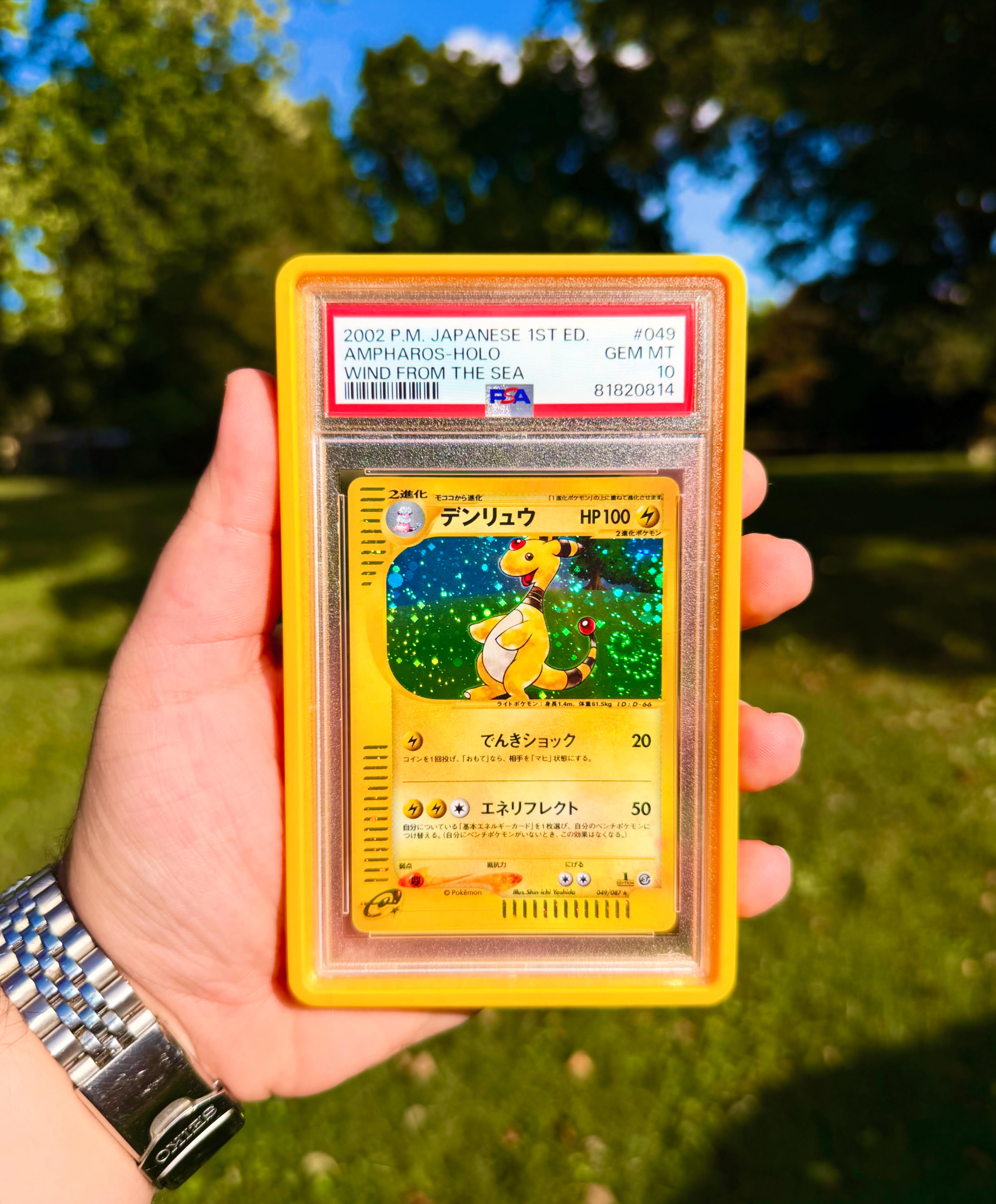 A hand holding a PSA 10 graded 2002 Japanese 1st Edition Ampharos holo card outdoors