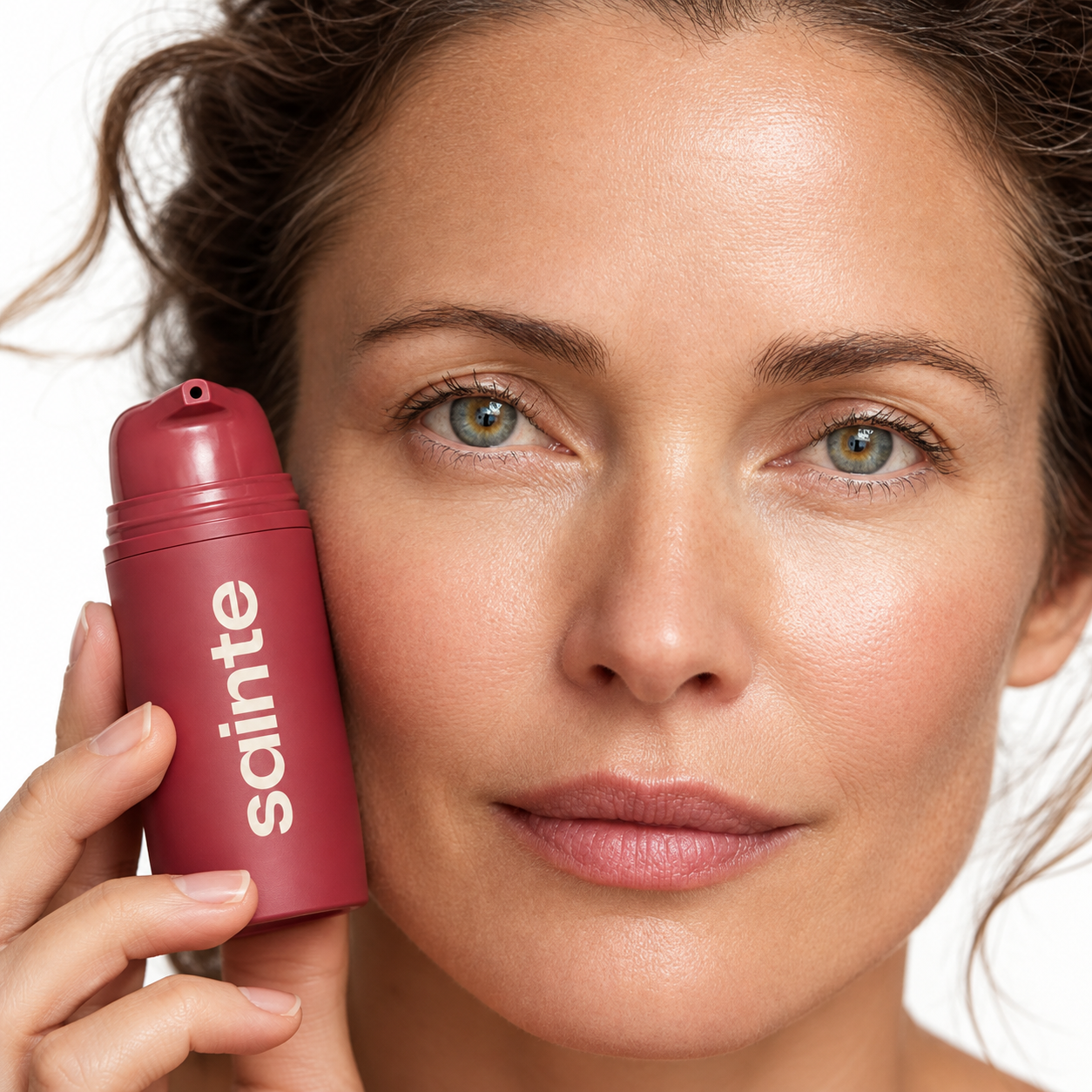 Mujer sosteniendo la base de maquillaje Sainte junto a su rostro