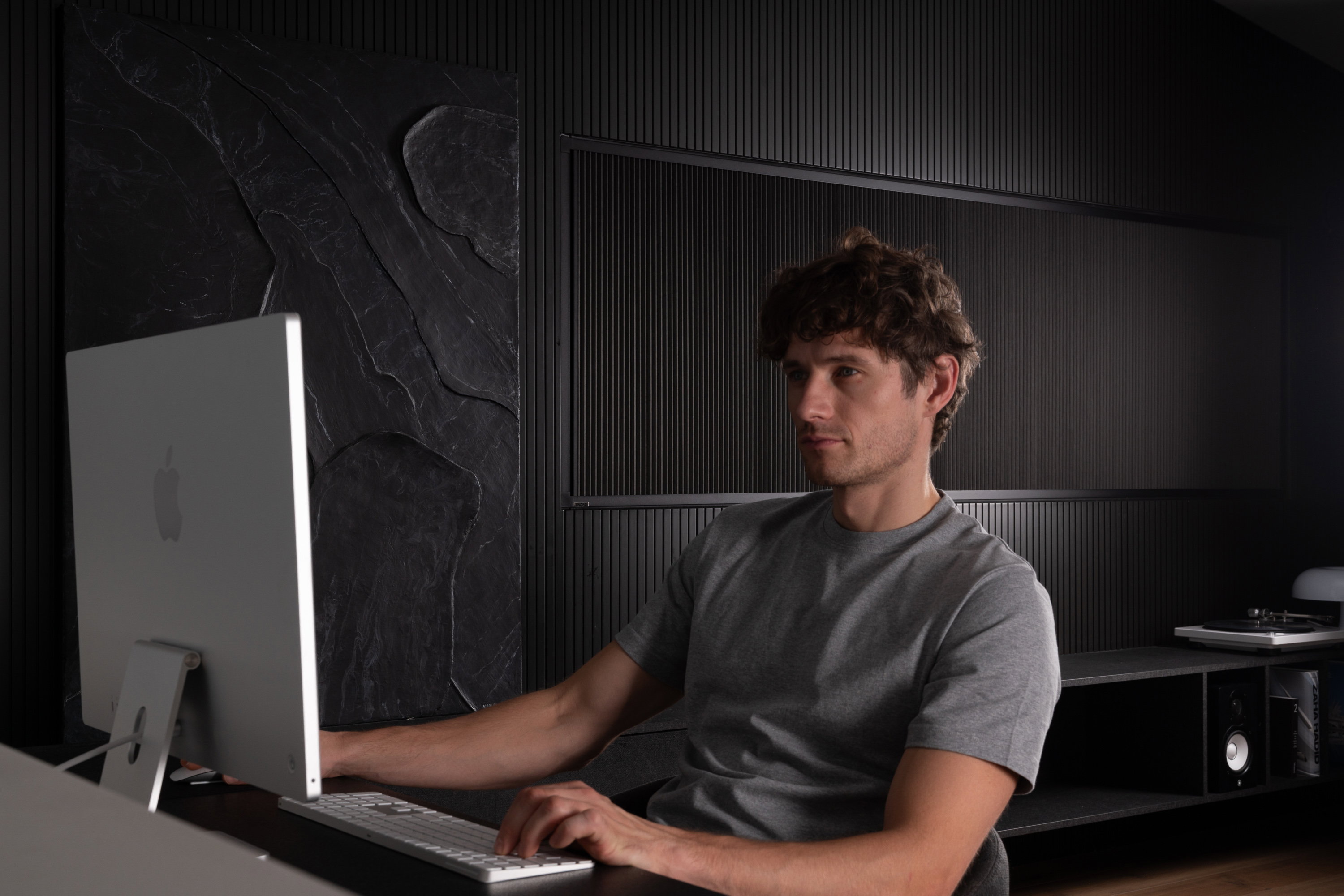 Creator working at a computer in a dark, minimalist home studio