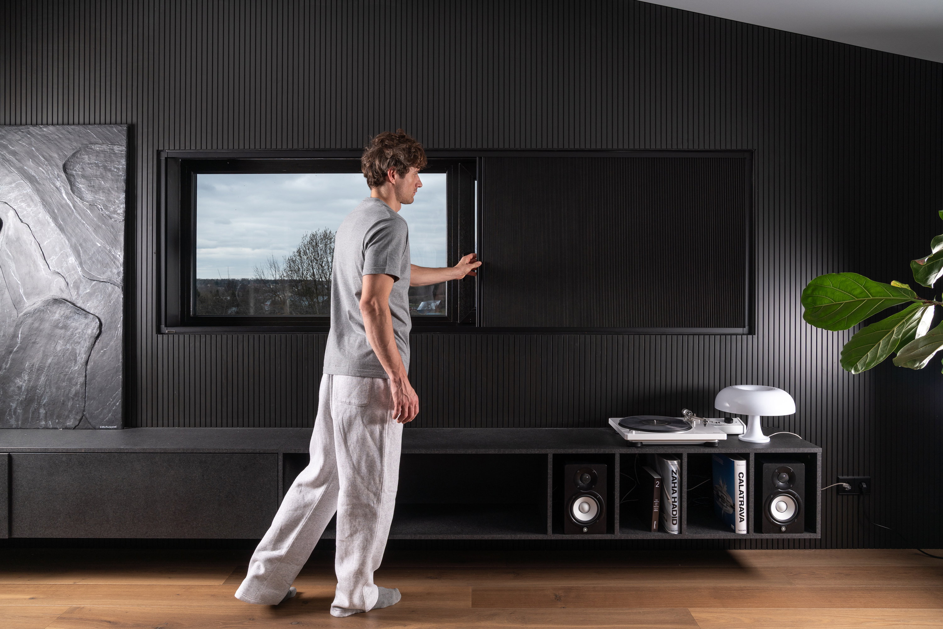 Man closing a Guard blackout blind on a window in a dark, slatted living room