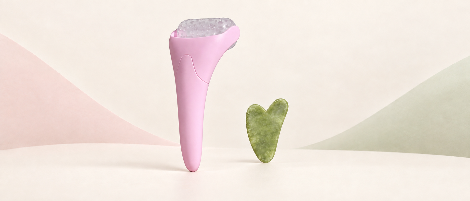 Rosa LUMA-isroller ved siden av en grønn hjerteformet gua sha-stein mot en kremhvit bakgrunn